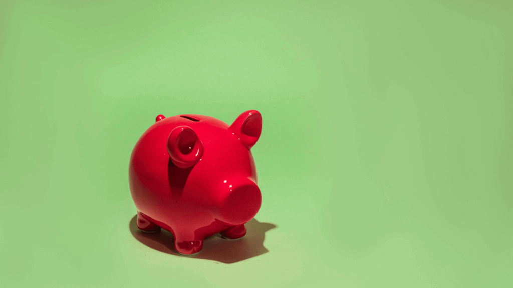 Red piggy bank on green background symbolizing saving money and building wealth through daily habits