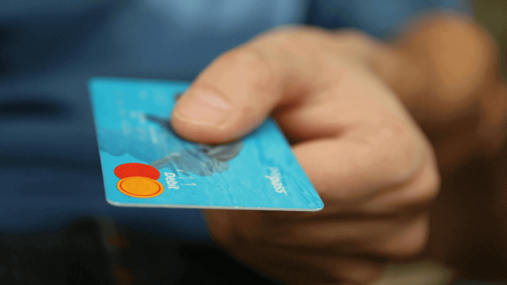 A hand holding a blue debit card, symbolizing overspending and credit dependency