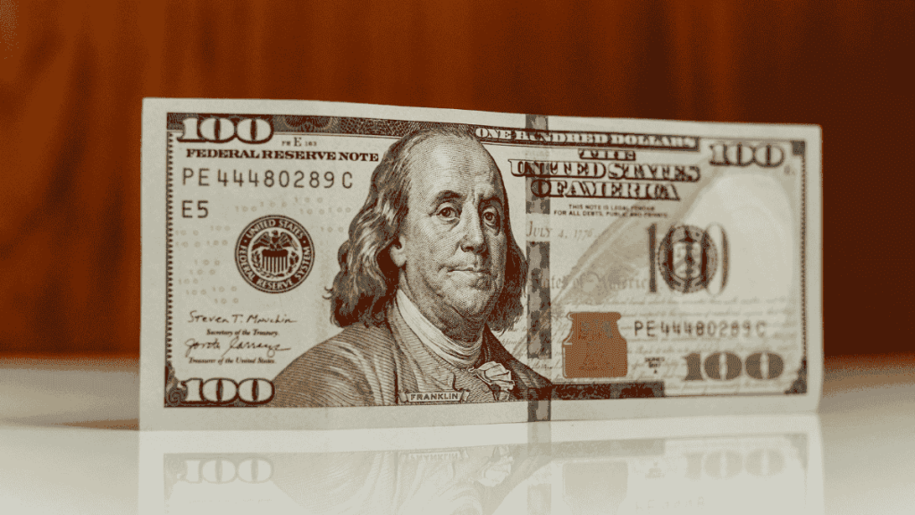 Crisp one hundred dollar bill standing on a reflective surface, symbolizing saving and building wealth