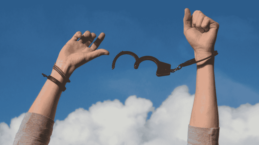 Hands breaking free from handcuffs under a blue sky, symbolizing personal freedom and taking back control of life.