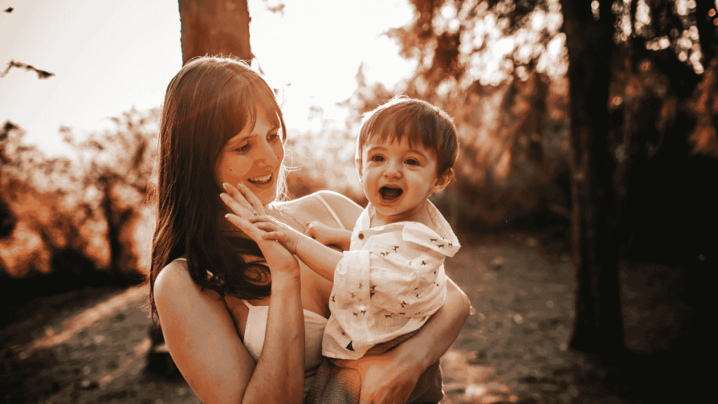 Smiling mother holding her happy toddler in a sunlit forest, symbolizing personal growth, connection, and intentional living.
